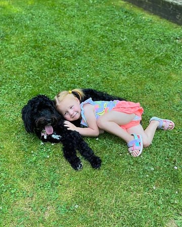 Little girl laying on grass with her black Australian Labradoodle